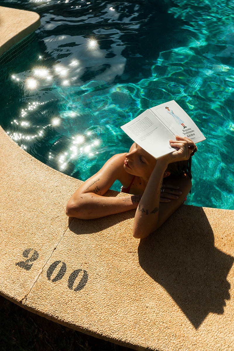 woman in pool, holding book to shed the sun