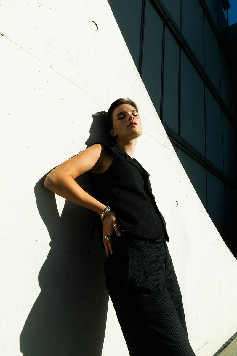 woman leaning against a building, wearing a black suit